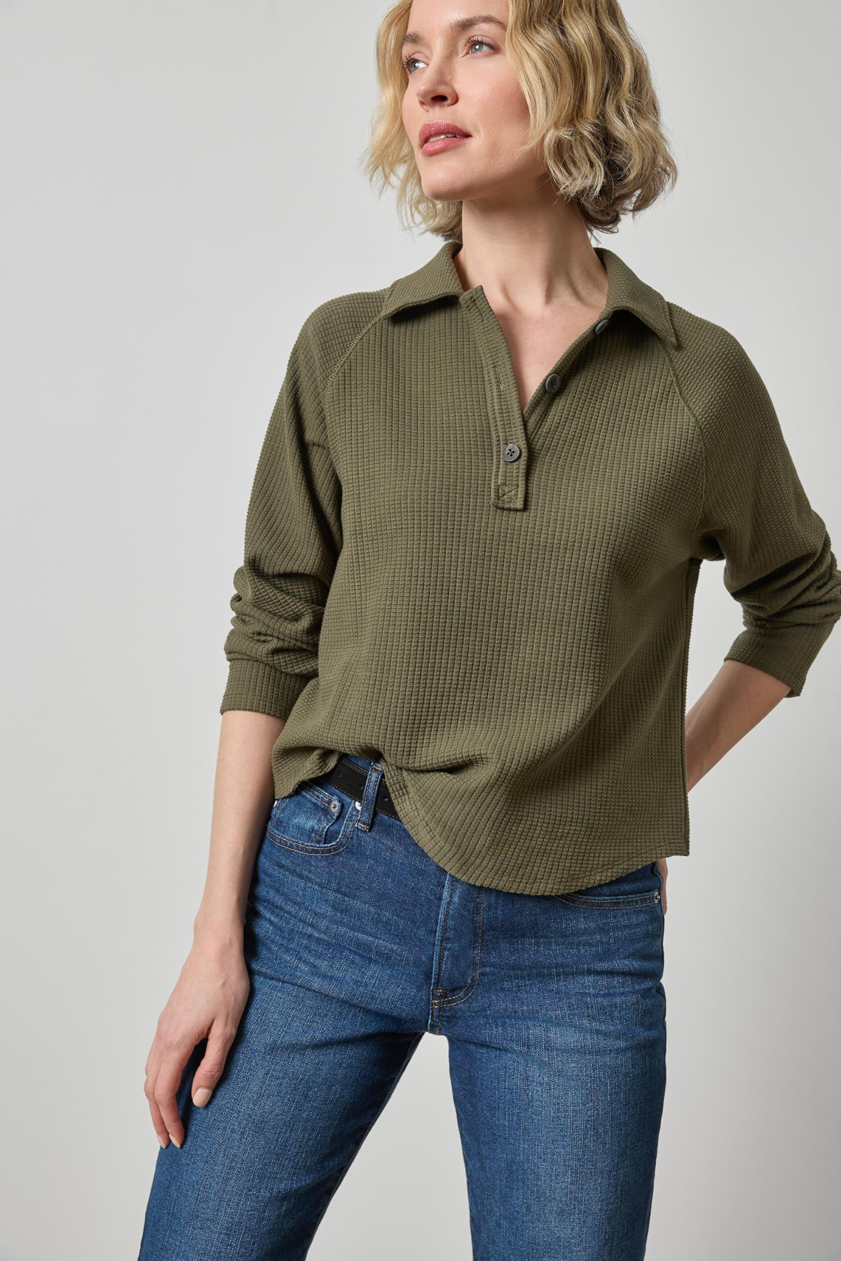 Woman wearing an olive green textured shirt and blue jeans on a gray background