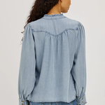 Woman wearing a light blue denim shirt and jeans on a plain background