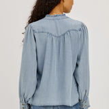 Woman wearing a light blue denim shirt and jeans on a plain background