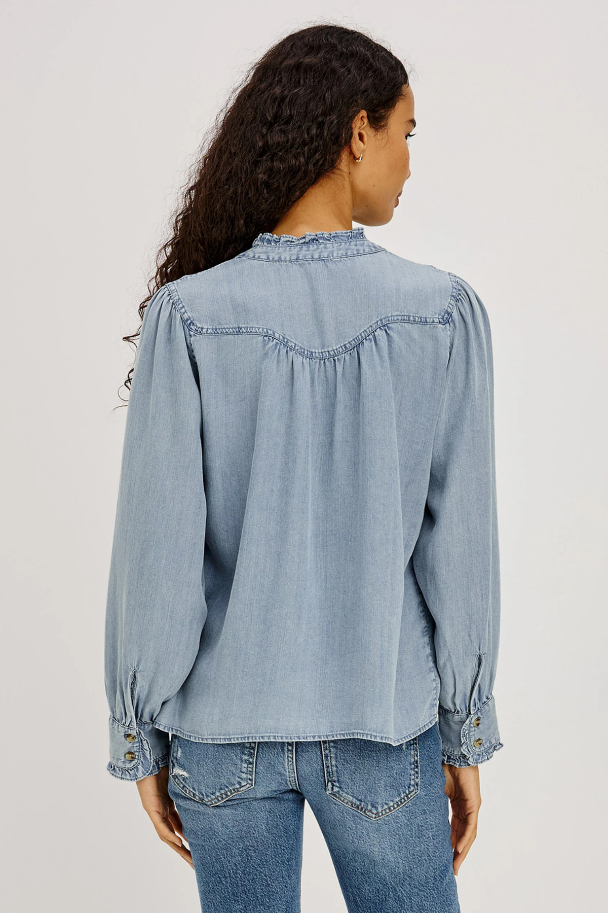 Woman wearing a light blue denim shirt and jeans on a plain background
