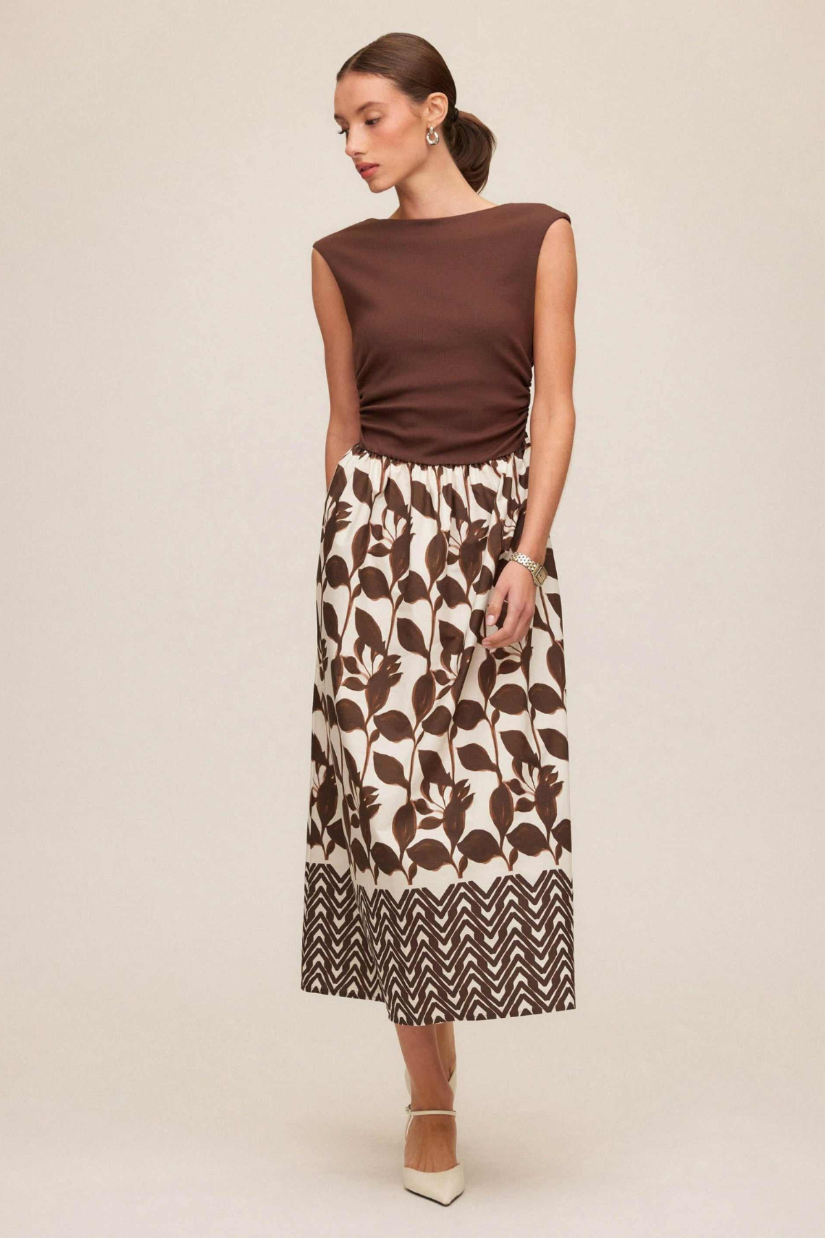 Woman wearing a brown top and patterned skirt on a beige background