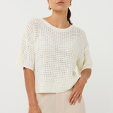 Woman wearing a white textured top and beige pants against a plain background