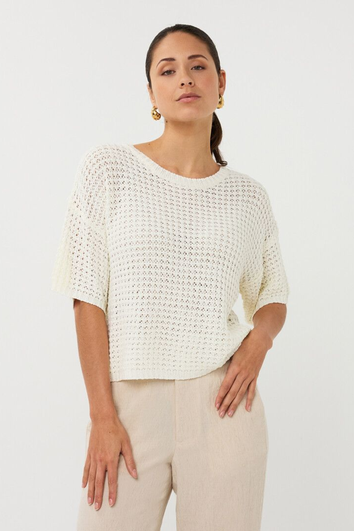 Woman wearing a white textured top and beige pants against a plain background