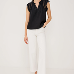 Woman wearing a black top and white pants on a plain background