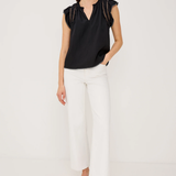 Woman wearing a black top and white pants on a plain background