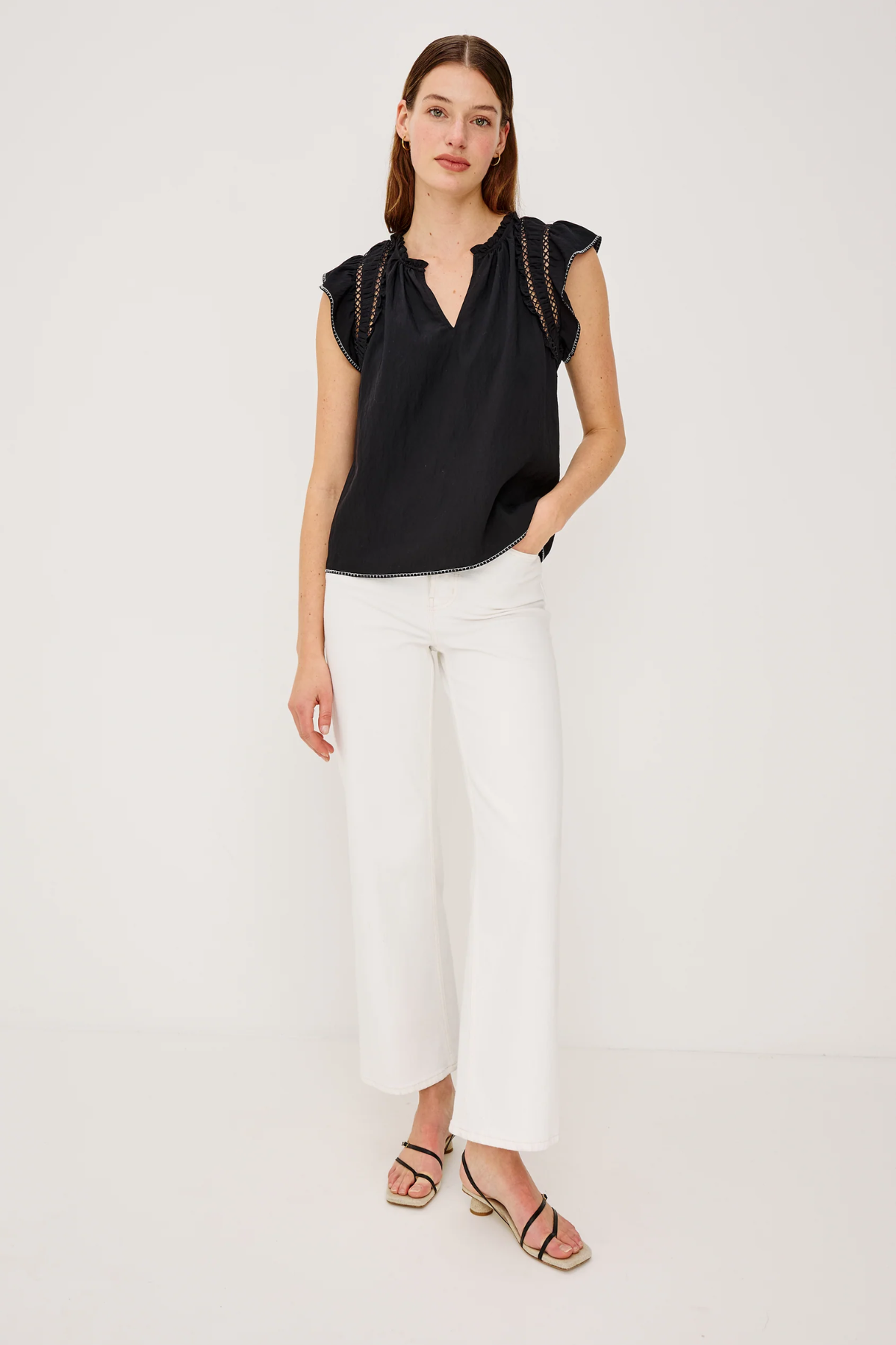 Woman wearing a black top and white pants on a plain background