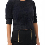 A woman wearing a dark navy fuzzy cropped sweater with three-quarter sleeves and black pants with gold zipper details, photographed against a plain white background.