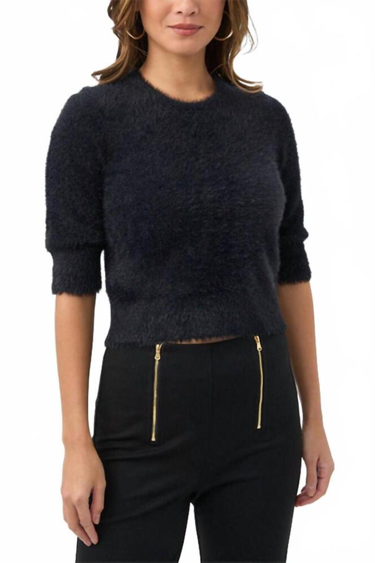 A woman wearing a dark navy fuzzy cropped sweater with three-quarter sleeves and black pants with gold zipper details, photographed against a plain white background.