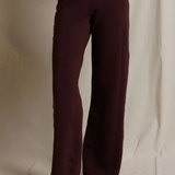 A person wearing dark burgundy wide-leg pants, shown from the waist down against a draped off-white fabric backdrop.