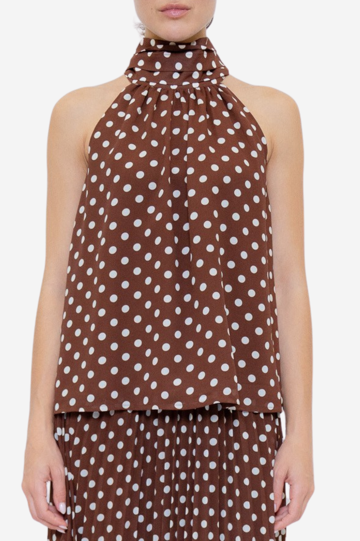 A model wearing a brown halter-neck top and matching pleated skirt set, both featuring a white polka dot pattern, against a plain light gray background.