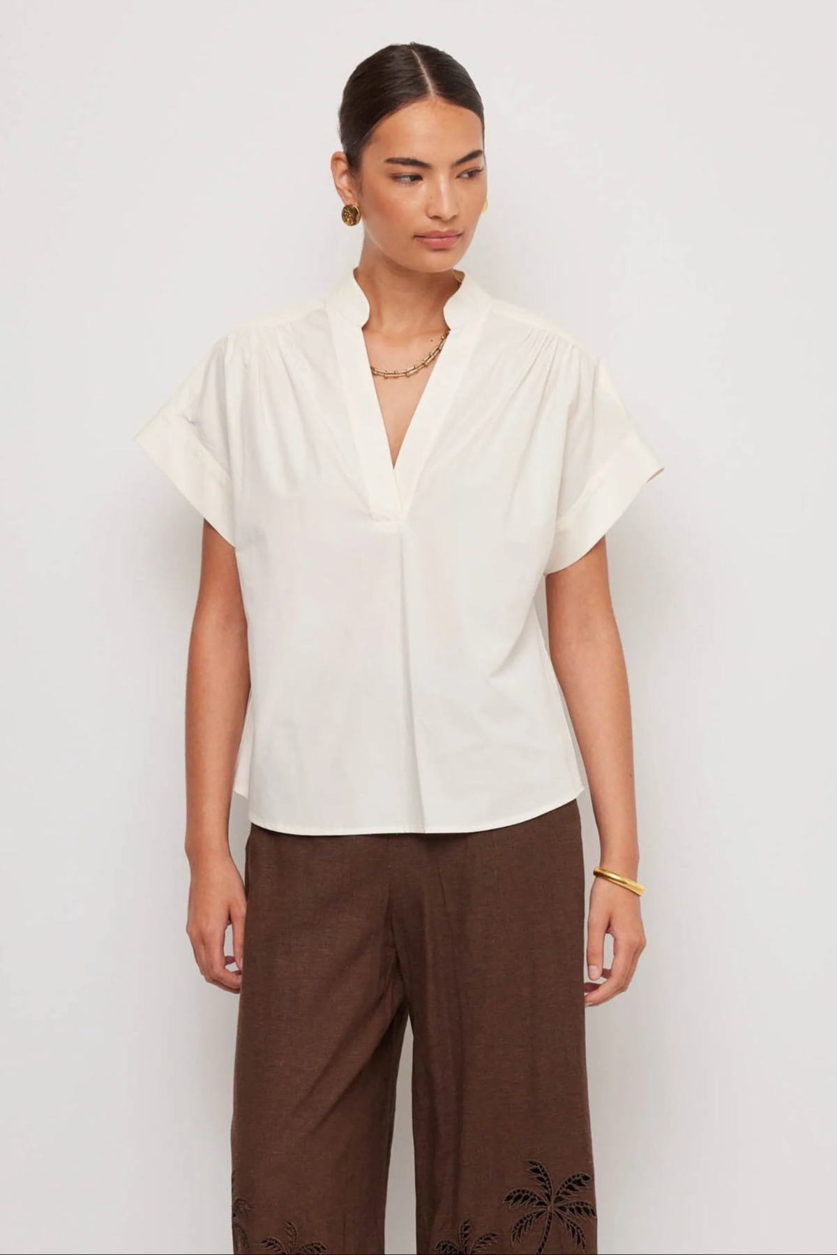 Woman wearing a white blouse and brown pants on a plain background
