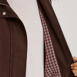 Close-up of a person wearing a dark brown jacket over a white t-shirt, with the jacket's zipper open to reveal a red and white checkered lining.