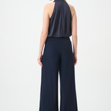 A woman shown from the back wearing a sleeveless navy top and matching wide-leg navy pants against a plain light gray studio background.
