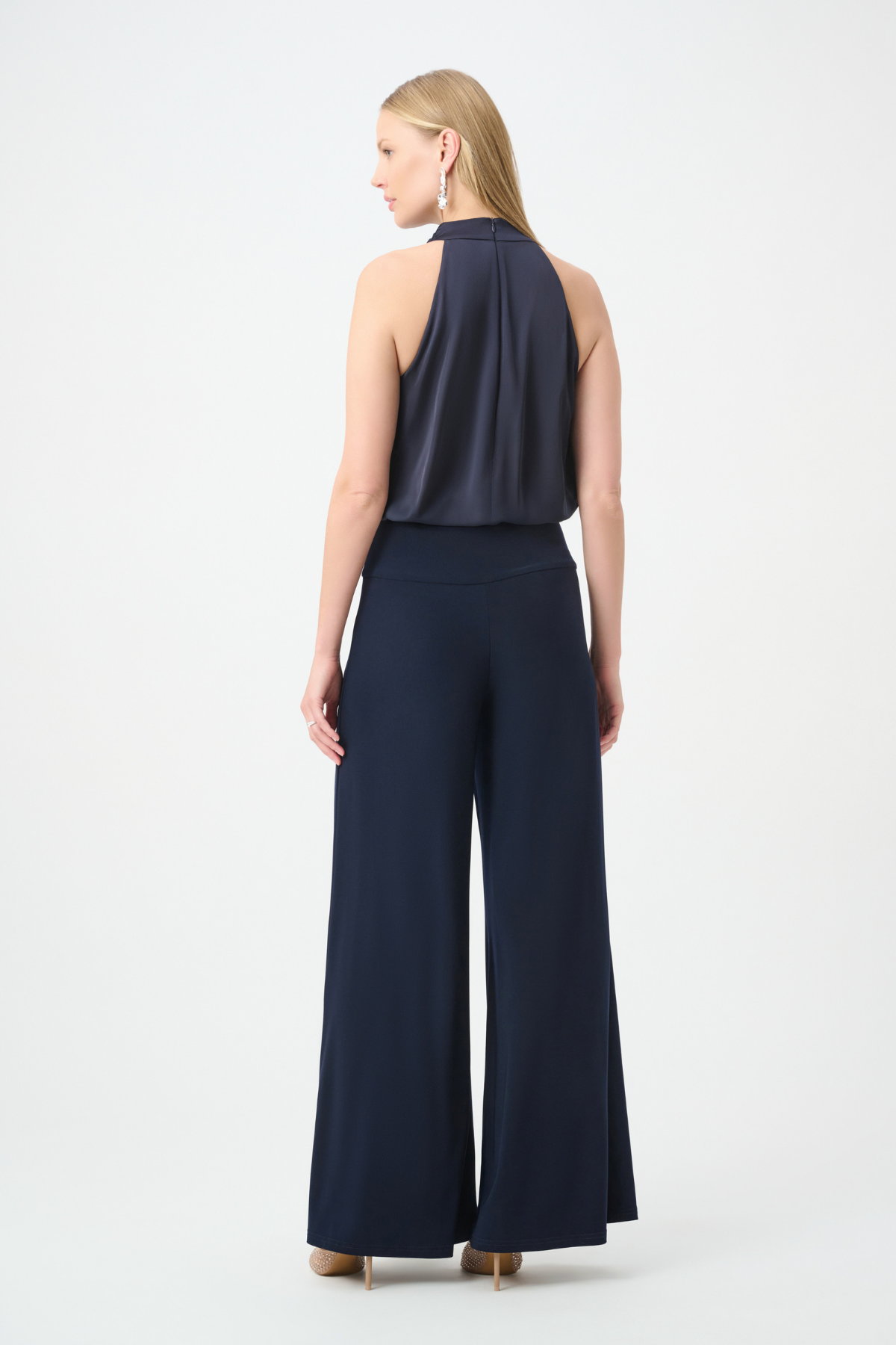 A woman shown from the back wearing a sleeveless navy top and matching wide-leg navy pants against a plain light gray studio background.