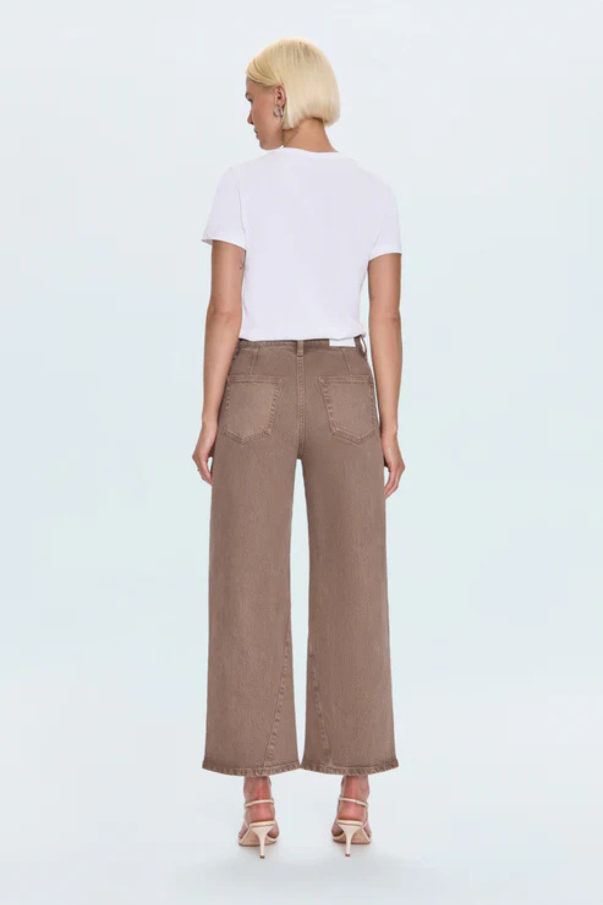 A model shown from the back wearing a white short-sleeve crop top and brown wide-leg cropped pants, paired with beige high-heeled sandals, against a light gray studio background.