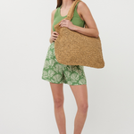 woman in green outfit on white background holding a beach tote
