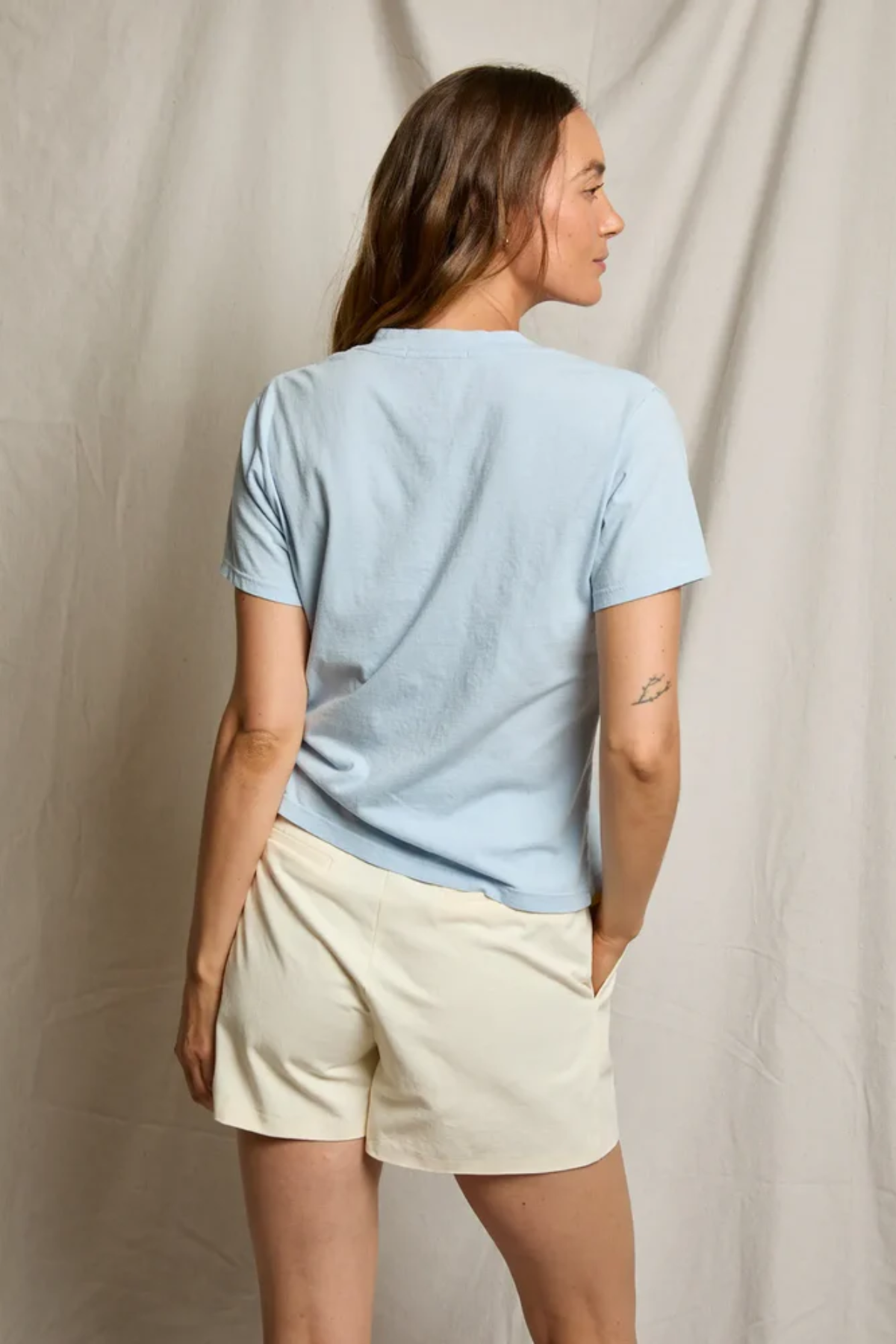 Woman wearing a light blue t-shirt and beige shorts against a neutral background