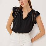 Woman wearing a black top with ruffled sleeves and white pants on a light background