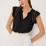 Woman wearing a black top with ruffled sleeves and white pants on a light background