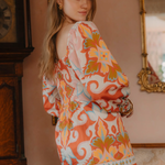 Woman wearing a colorful patterned dress in an indoor setting with a mirror and clock.