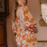 Woman wearing a colorful patterned dress in an indoor setting with a mirror and clock.