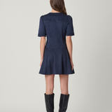 A woman viewed from the back wearing a short-sleeve navy blue mini dress and black knee-high boots, standing against a light gray studio background.