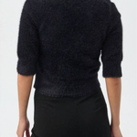 A woman shown from the back wearing a dark fuzzy knit sweater with three-quarter sleeves and black pants, against a plain white studio background.