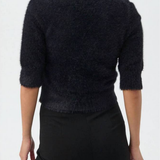 A woman shown from the back wearing a dark fuzzy knit sweater with three-quarter sleeves and black pants, against a plain white studio background.