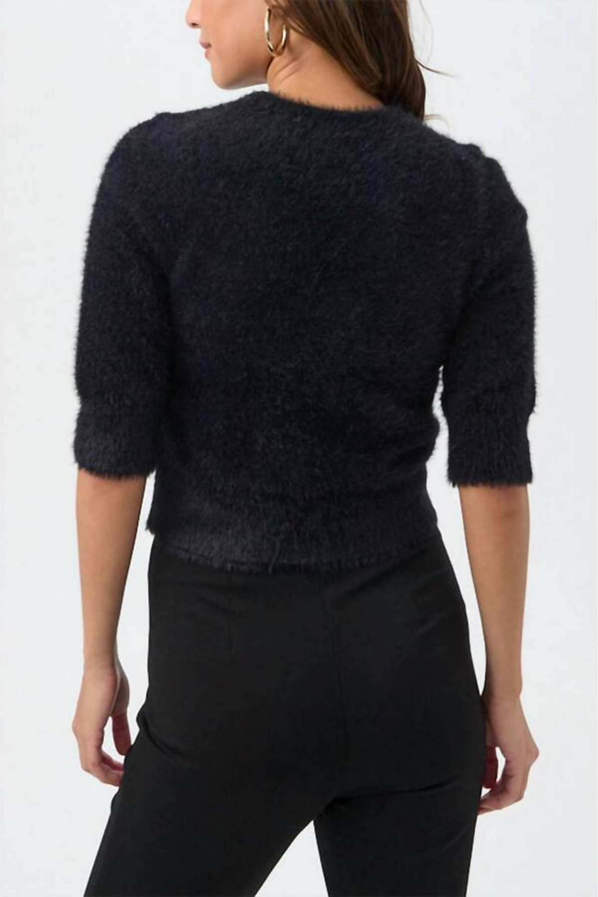 A woman shown from the back wearing a dark fuzzy knit sweater with three-quarter sleeves and black pants, against a plain white studio background.