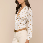 Woman wearing a white blouse with gold heart patterns and beige pants on a beige background