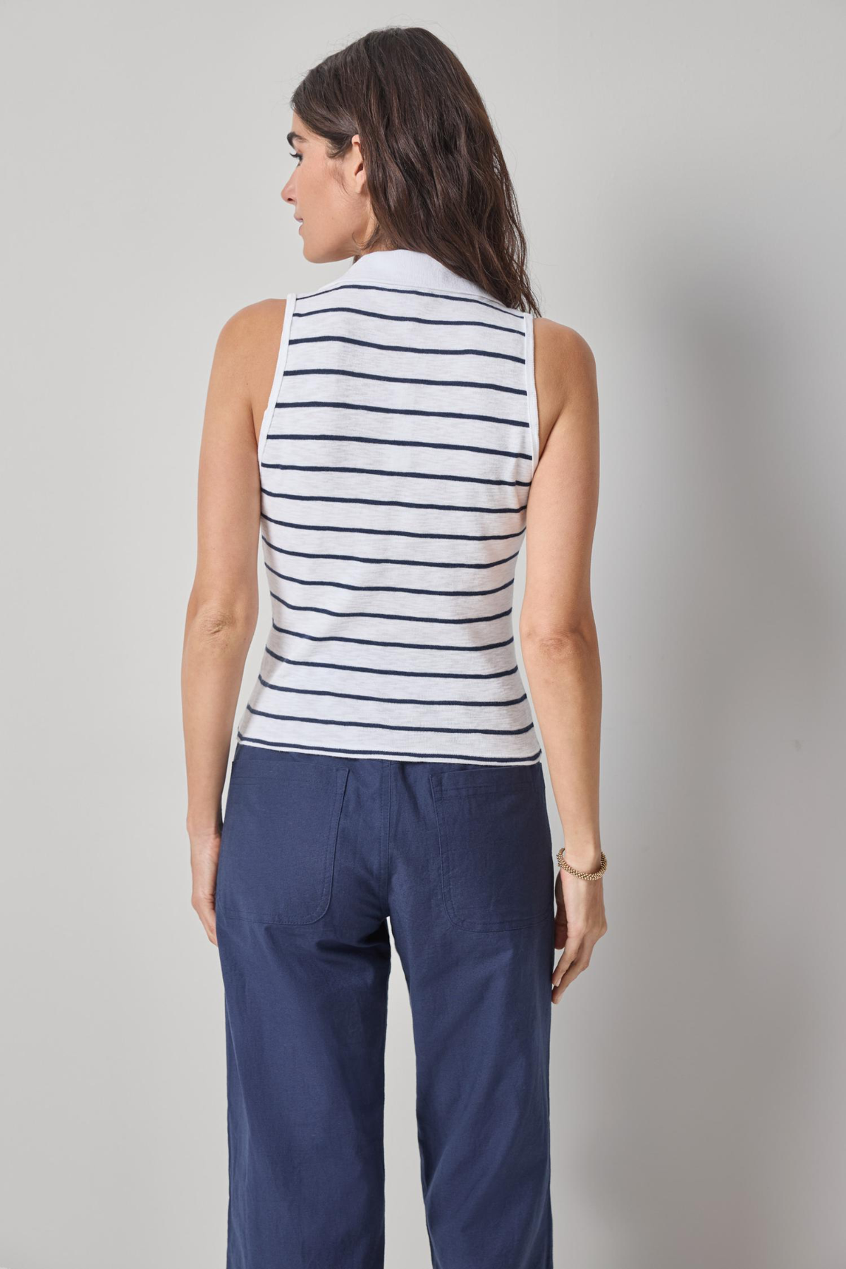 Woman wearing a striped sleeveless top and blue pants against a plain background