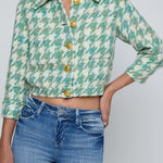 Person wearing a green patterned jacket with gold buttons and blue jeans on a light gray background