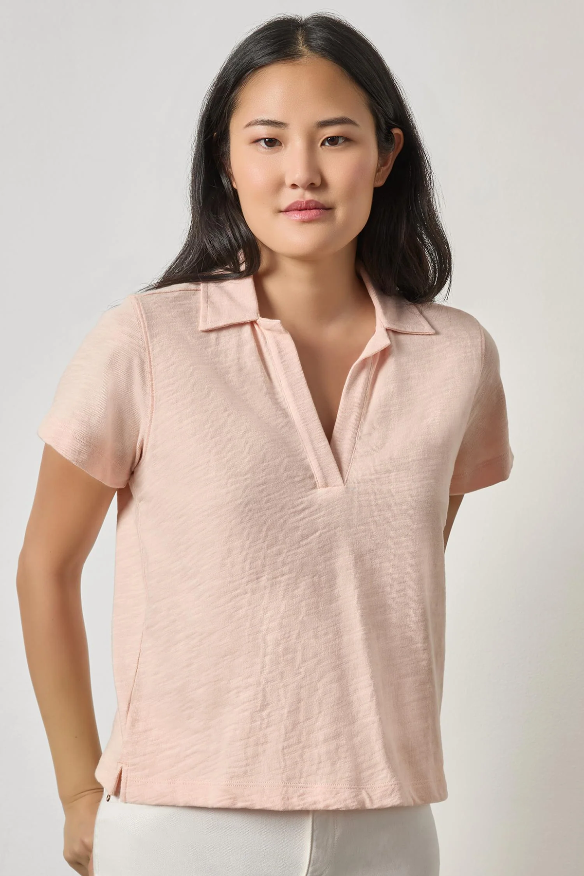 Woman wearing a light pink short-sleeve blouse against a plain background