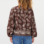 A person viewed from the back wearing a brown long-sleeve blouse with a beige paisley pattern, paired with blue jeans, against a plain white background.
