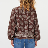 A person viewed from the back wearing a brown long-sleeve blouse with a beige paisley pattern, paired with blue jeans, against a plain white background.