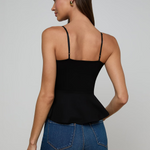 Woman wearing a black tank top and blue jeans on a plain background