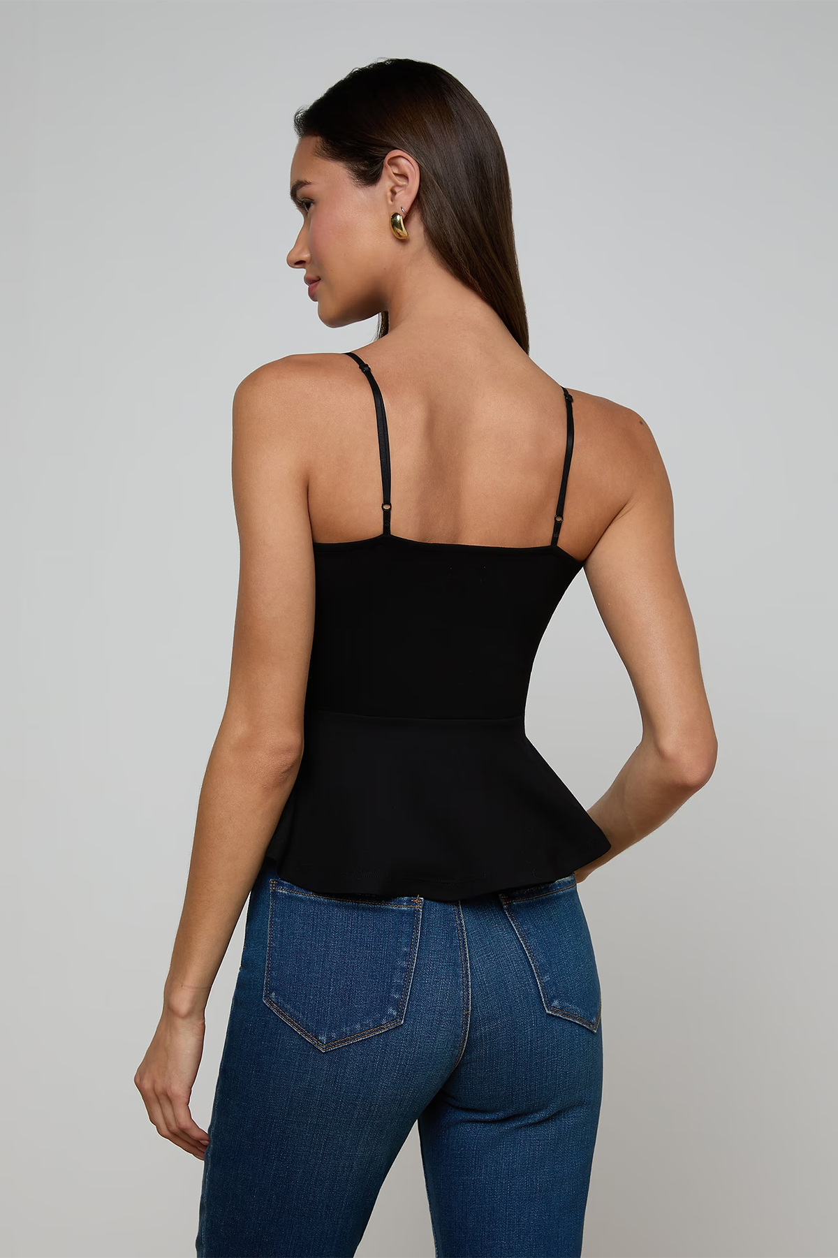 Woman wearing a black tank top and blue jeans on a plain background