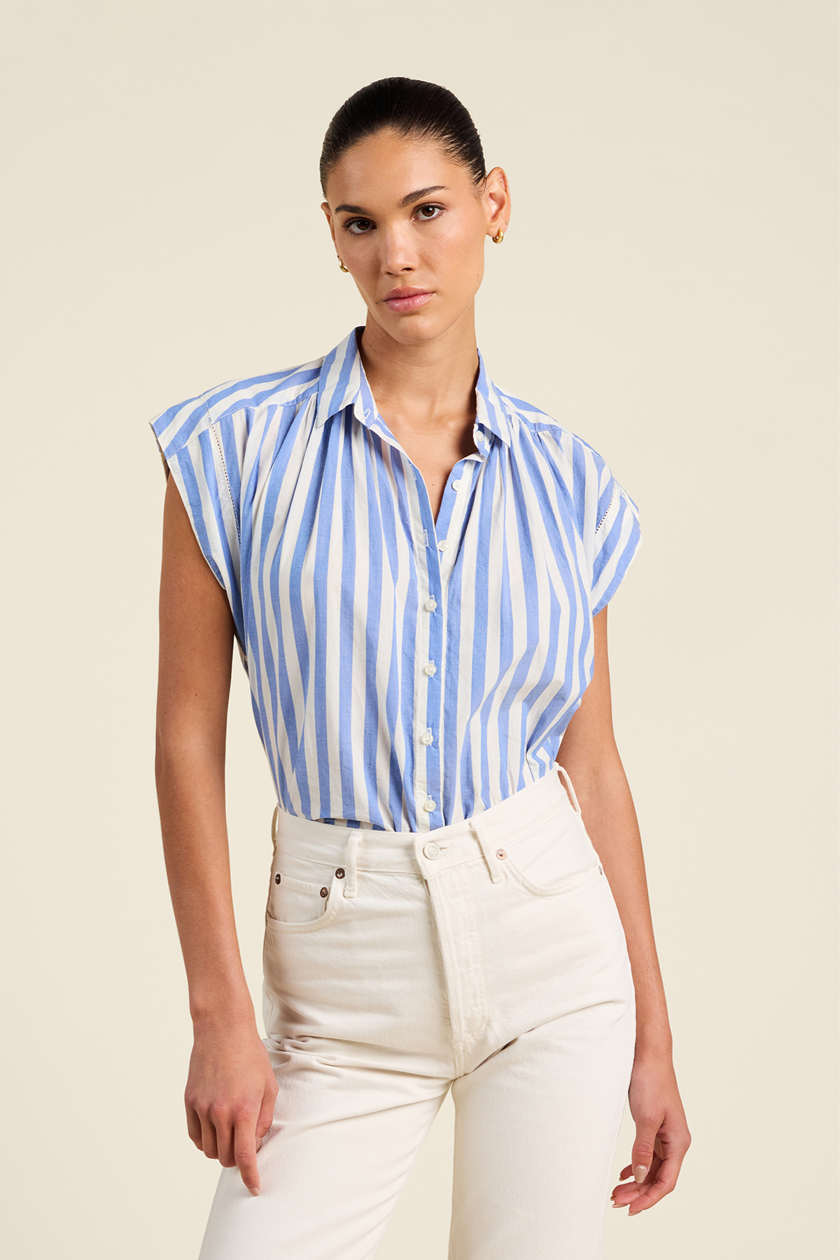 Woman wearing a blue and white striped shirt with white pants on a beige background