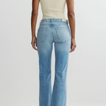 Person wearing a beige sleeveless top and blue flared jeans on a light gray background