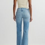 Person wearing a beige sleeveless top and blue flared jeans on a light gray background