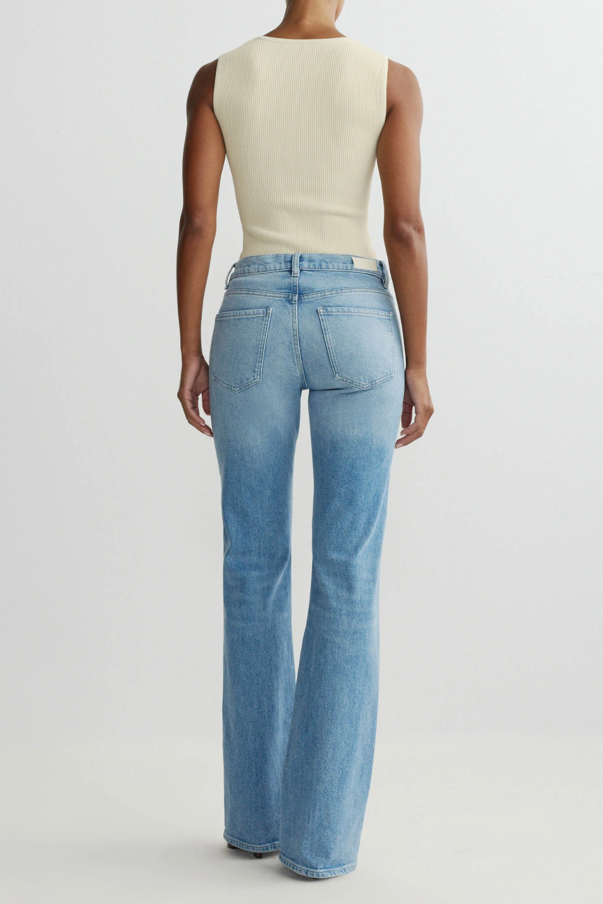 Person wearing a beige sleeveless top and blue flared jeans on a light gray background