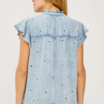 Woman wearing a light blue denim top with ruffled sleeves on a white background