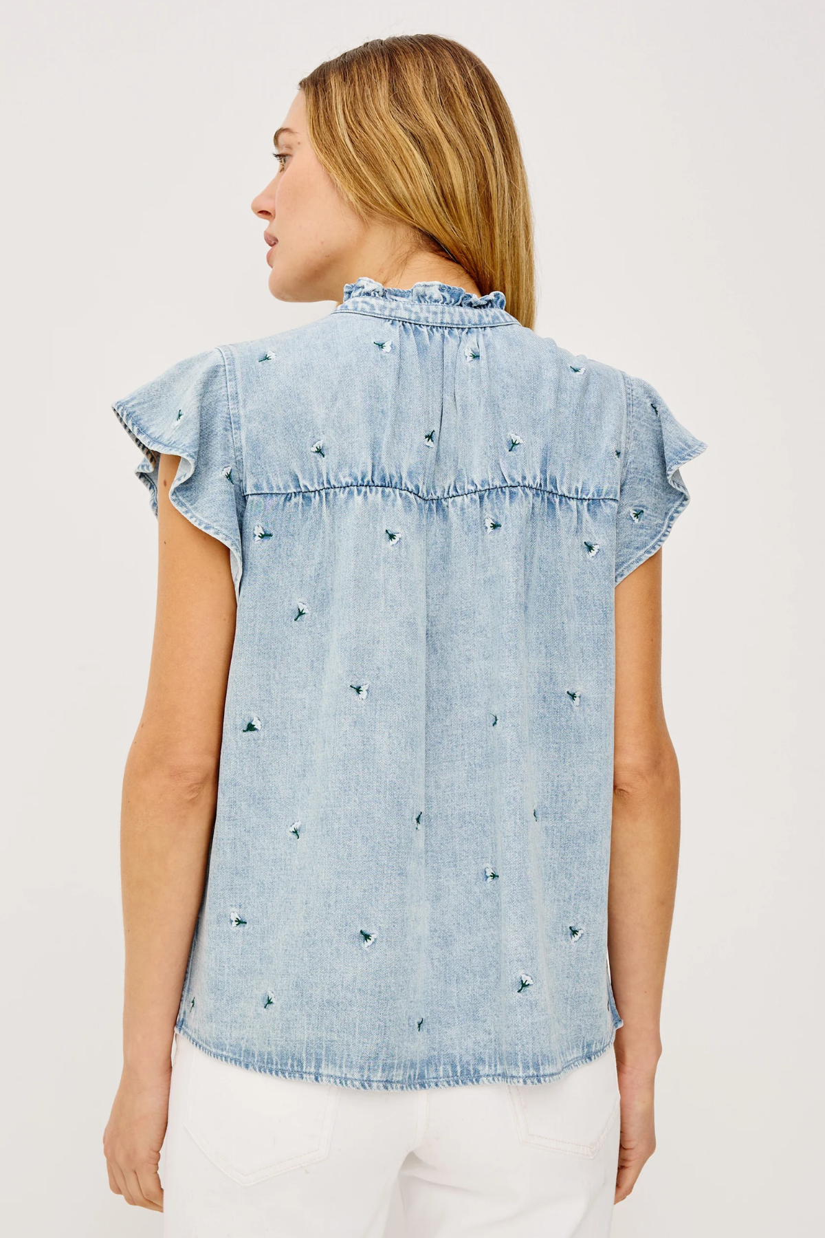 Woman wearing a light blue denim top with ruffled sleeves on a white background