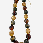 A beaded necklace made of polished round stone beads in earthy brown, amber, green, and black tones, with a small gold chain extender, shown on a light gray background.