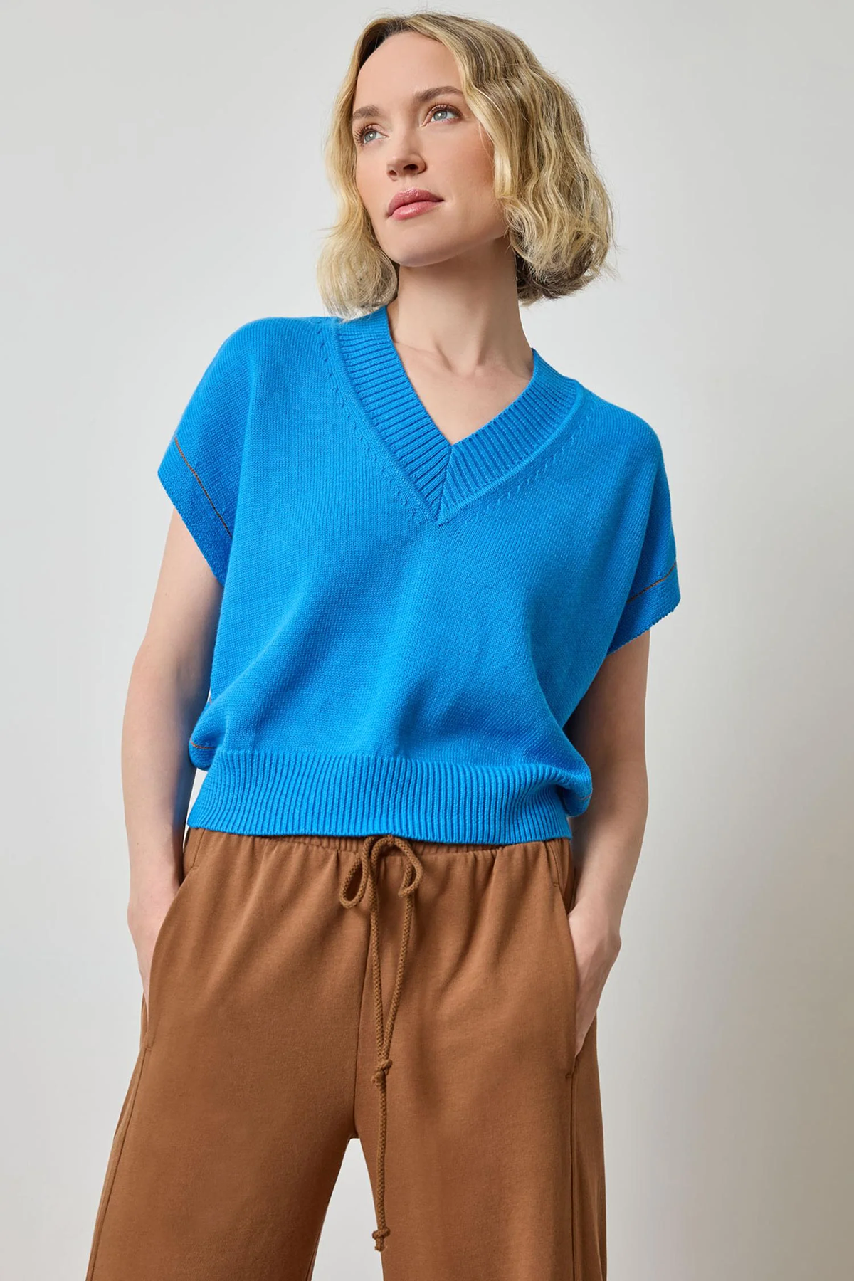 Woman wearing a blue sweater and brown pants against a plain background